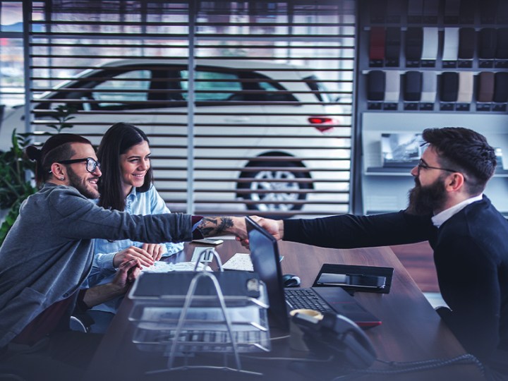 two car buyers and a dealership salesperson closing a deal