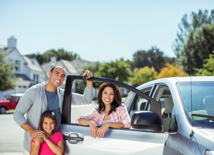 A family in front of the new car that has been delivered to their driveway